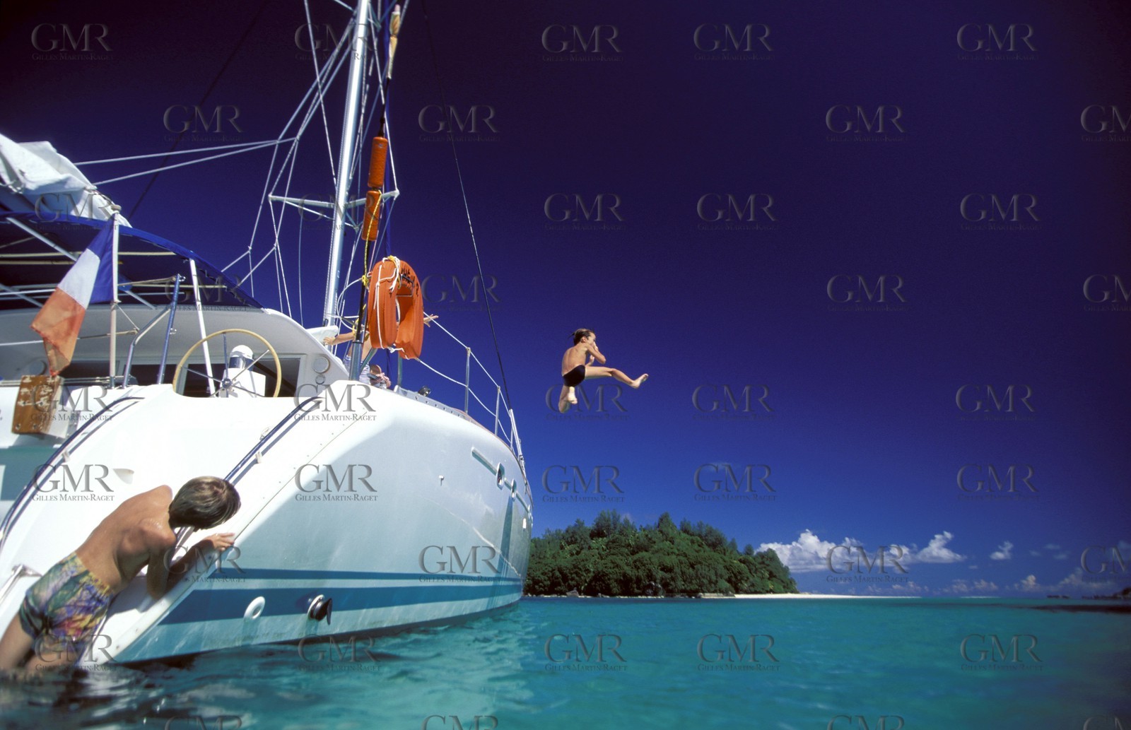 Boy jumping off the side of a catamaran into the sea